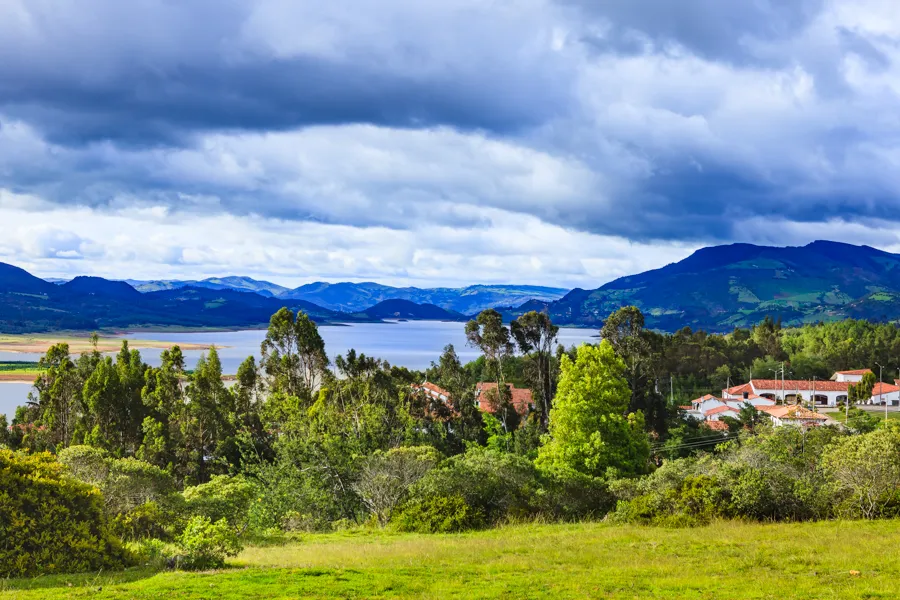 The Embalse de Tominé seen across pasture and eucalyptus trees, with blue hills beyond and heavy cloud overhead