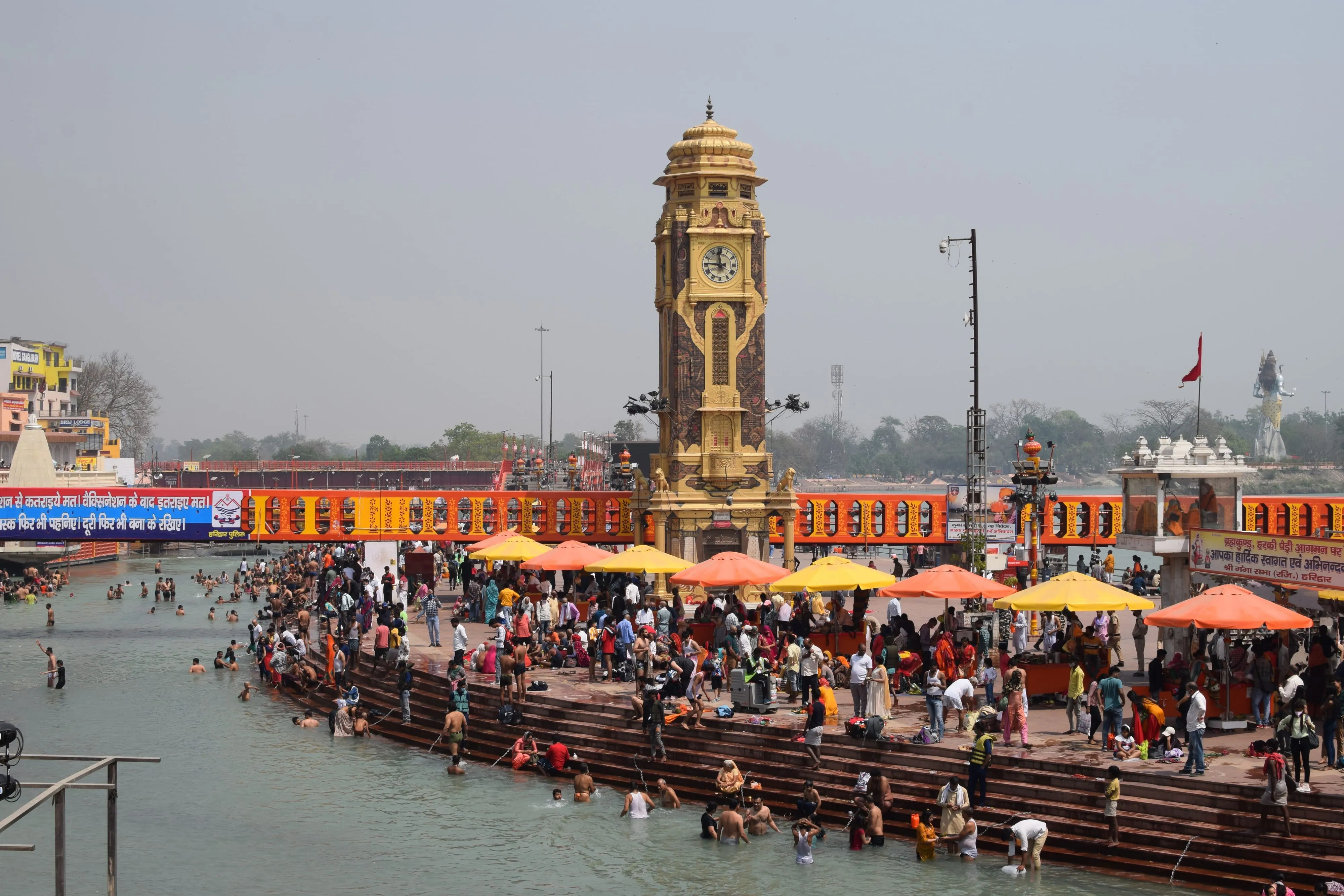 Pilgrims bathing in the Ganges at Har Ki Pauri in Haridwar, with the ghat's clock tower and crowds along the steps