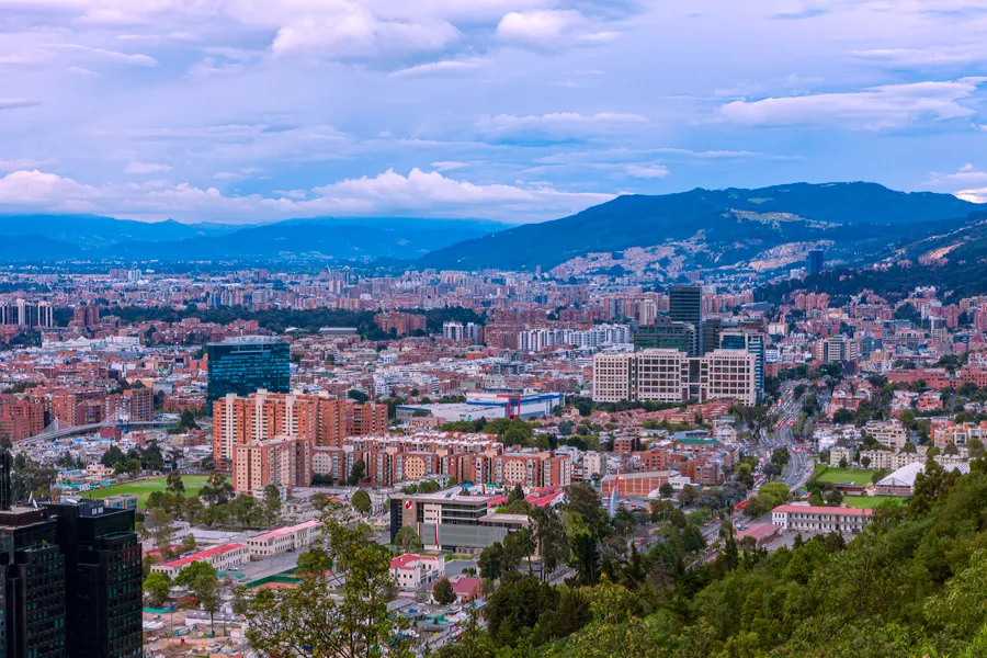 The northern districts of Bogotá spread out below a hillside road, with the Andes rising behind under evening cloud