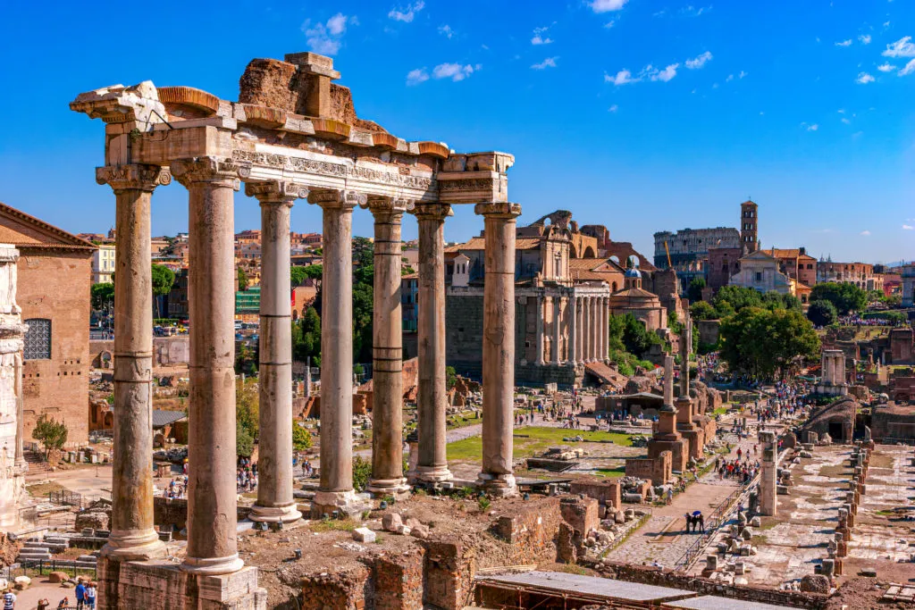 The eight surviving columns of the Temple of Saturn above the Roman Forum, with the Colosseum in the distance