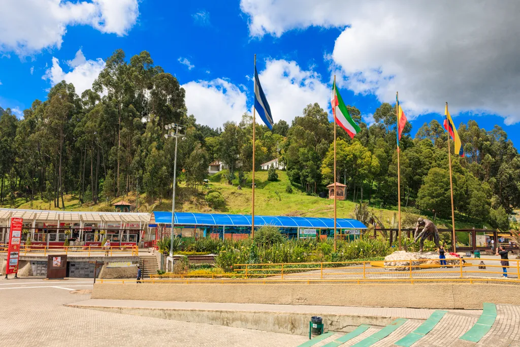 The Plaza del Minero at the entrance to the Zipaquirá salt mine, with flagpoles, a miner's statue, and wooded hills behind