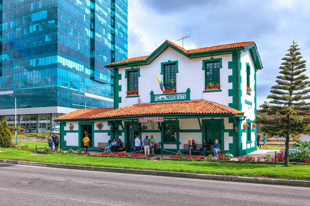 The green and white colonial railway station at Usaquén in Bogotá, with a modern glass tower rising behind it